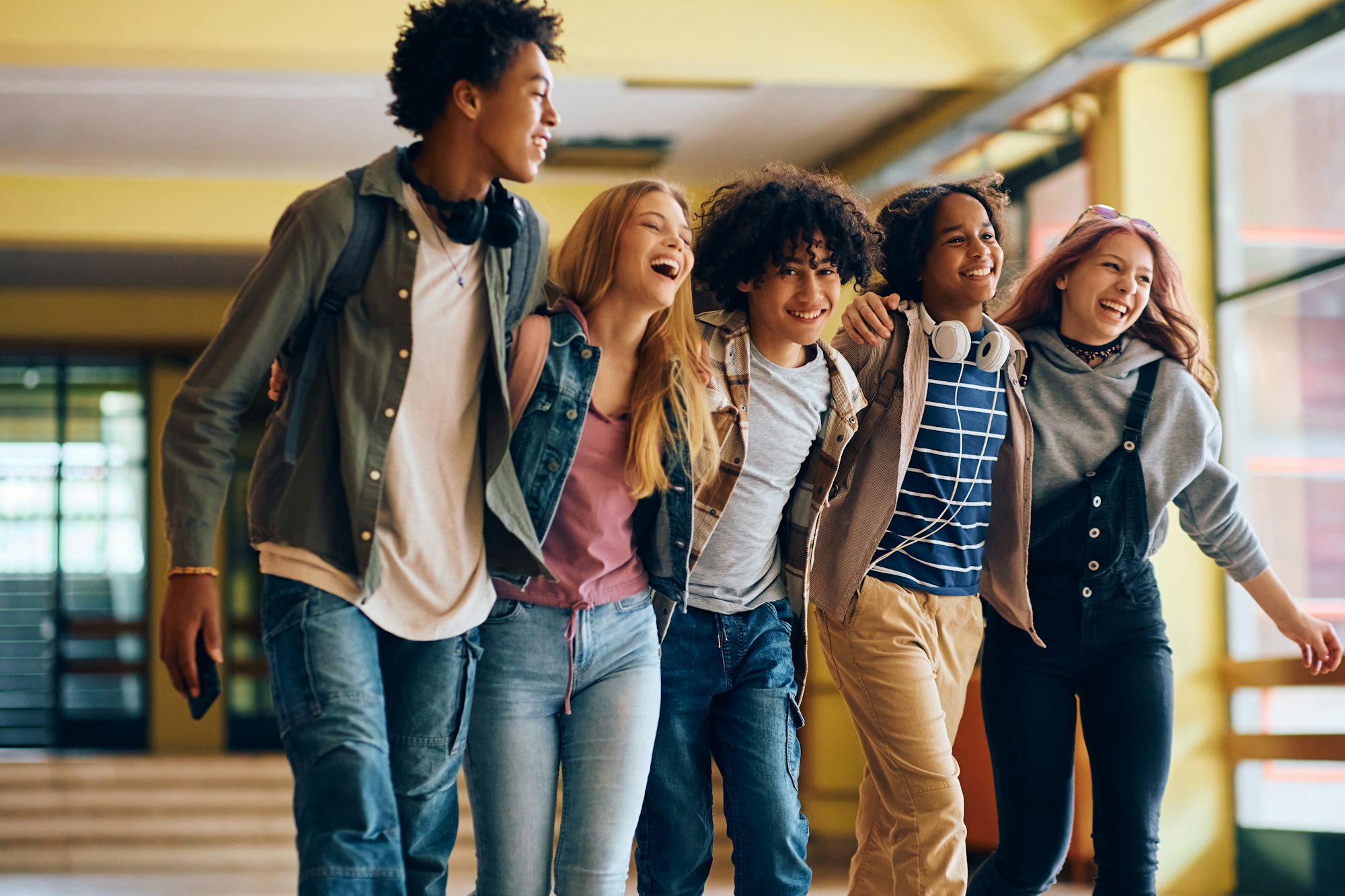 Multiracial group of cheerful high school friends walking through hallway at school.